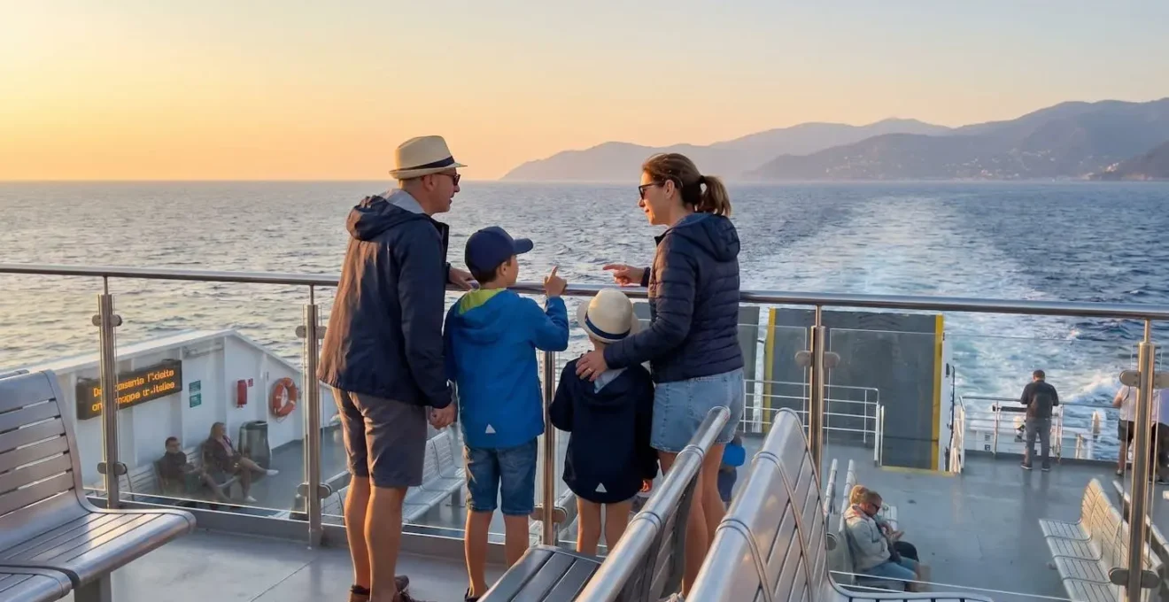 Una famiglia italiana vista di spalle osserva il mare al tramonto dal ponte esterno di un traghetto moderno