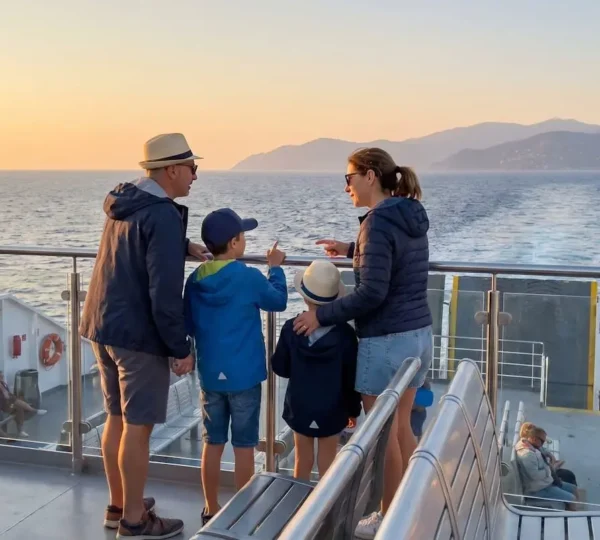 Una famiglia italiana vista di spalle osserva il mare al tramonto dal ponte esterno di un traghetto moderno