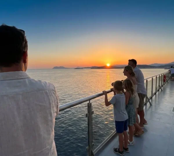 Una famiglia vista di spalle sulla prua di un traghetto moderno al tramonto, che osserva l'orizzonte del Mediterraneo con atmosfera serena
